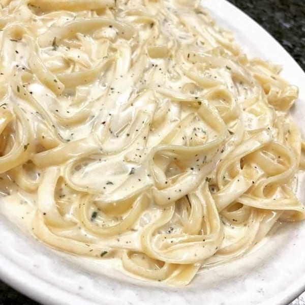 Fettuccine pasta with creamy Alfredo sauce and herbs on a white plate.
