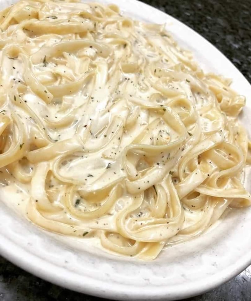 Fettuccine pasta with creamy Alfredo sauce and herbs on a white plate.