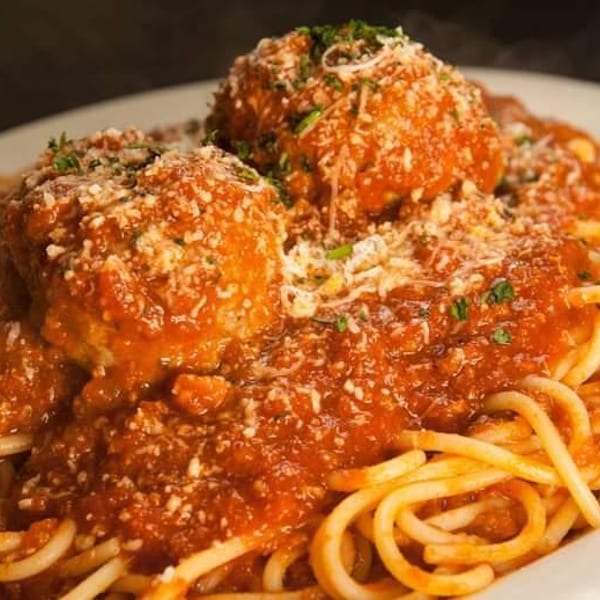Spaghetti and meatballs covered in red sauce, parmesan cheese, and fresh parsley on a white plate.