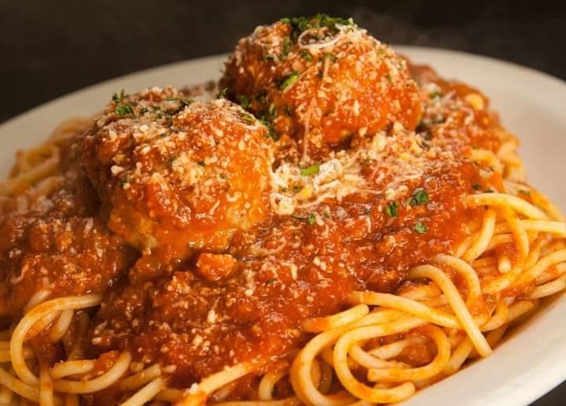 Spaghetti and meatballs covered in red sauce, parmesan cheese, and fresh parsley on a white plate.